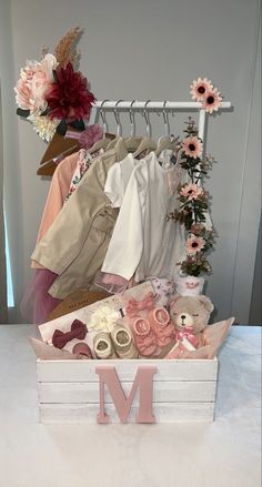 a wooden box filled with clothes and flowers on top of a white table next to a letter m