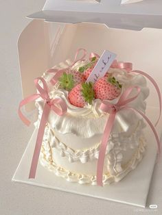 a white cake with strawberries on top and pink ribbon around the edges in a box