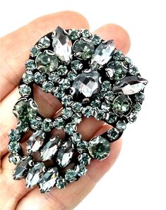 a hand holding a brooch with lots of stones in it's center,