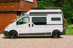 a small white van parked in front of a brick building next to a green field