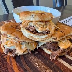 a pile of sandwiches sitting on top of a wooden cutting board next to a bowl