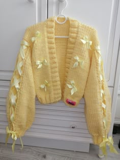 a yellow sweater with bows on it is hanging from a hook in front of a white door