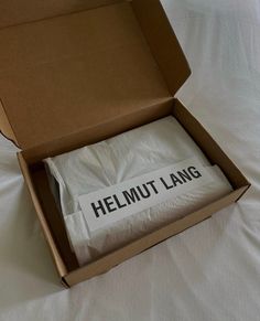 an open cardboard box on a bed with a sign in it that says helmut lang