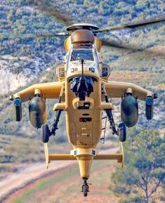 a yellow helicopter flying over a lush green hillside