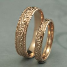 two gold wedding bands with intricate designs on them, set against a gray background in close proximity to each other