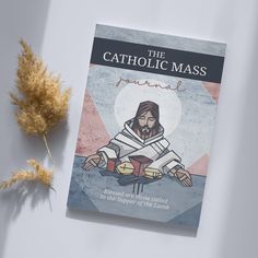 the catholic mass book next to a dried plant on a white surface with an illustration of jesus