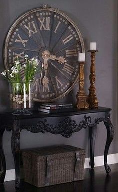 a clock on the wall above a table with vases and flowers in front of it