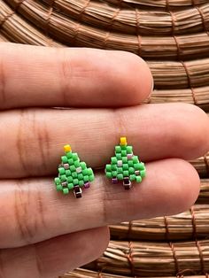 a hand holding two small green and yellow christmas trees on it's fingers,