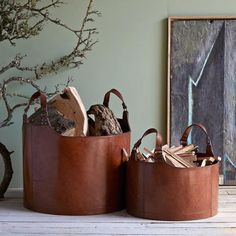 two brown leather baskets sitting on top of a wooden table next to a painting and tree