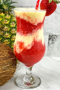 a red and white drink in a glass next to a pineapple