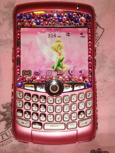 a pink cell phone with tinkerbells on the front and sides, sitting on a bed