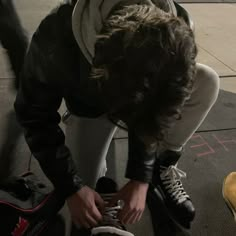 a person bending over on the ground with their shoes in front of them and one hand holding a shoelace