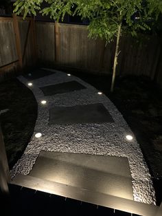 a walkway lit up at night with lights on the ground and trees in the background