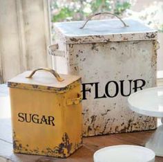 an old fashioned flour box, cake plate and sugar container sitting on a wooden table