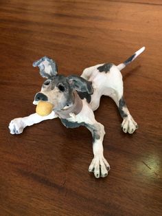 a toy dog laying on the floor with a ball in its mouth