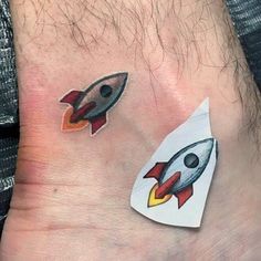 two small tattoos on the foot of a man with a rocket ship and space shuttle