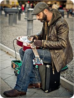 a man sitting on top of a suitcase holding a guitar