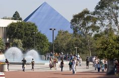 many people are walking around in front of a building with a blue pyramid behind it