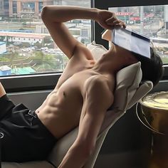 a shirtless man laying on top of a couch next to a window with cityscape in the background