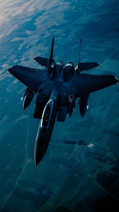 a fighter jet flying through the air over land and water in front of an airplane