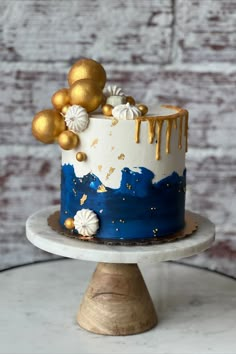 a blue and white cake with gold decorations on top is sitting on a small stand