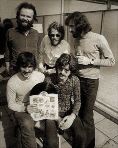 black and white photograph of five people sitting on a bench, one holding a sign