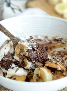 a white bowl filled with ice cream and banana slices covered in toppings on top of a table