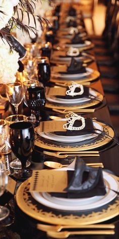 a long table is set with black and gold place settings for formal dinnereons