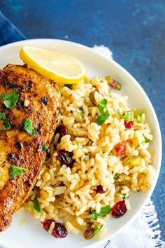 a white plate topped with rice and chicken next to a lemon wedge on top of a table