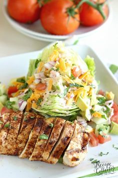 grilled chicken, lettuce and tomato salad on a white plate with tomatoes in the background