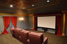 an empty theater with red drapes and two recliners in front of the screen