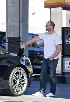 a man standing next to a car at a gas station with his hand on the fuel pump