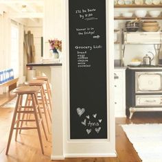 a kitchen with white walls and wooden flooring next to an open door that has a chalkboard on the wall