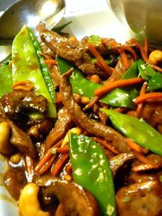 a white plate topped with meat and veggies next to a spoon on top of a table