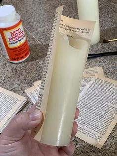 a person holding an open book in their left hand and some papers on the table next to them