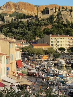 boats are docked in the water near buildings and hills with trees on top of them