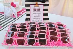 a table topped with lots of pink sunglasses on top of a white table covered in pink frosting