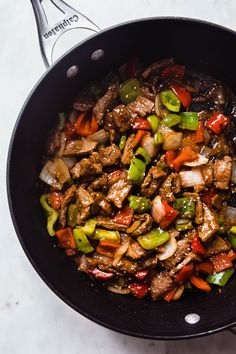 a skillet filled with meat and vegetables on top of a white counter next to utensils