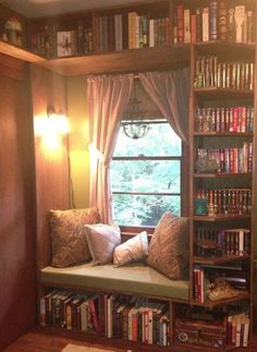 a window seat in front of a bookshelf filled with lots of books and pillows