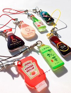 several different colored bottles are on a white surface with red string attached to the keychain