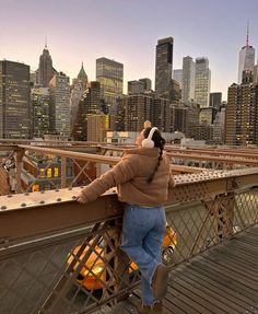 a man standing on top of a bridge next to a tall city skyline at sunset