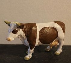 a brown and white toy cow standing on top of a table next to a wall