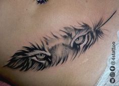 a woman's stomach with an eye and feather tattoo on the side of her stomach