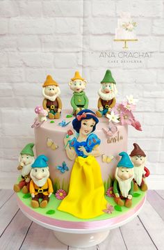 a cake decorated with snow white and seven dwarfs sitting on top of it, surrounded by other figurines