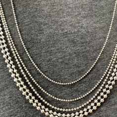 a woman wearing a long chain necklace with silver beads on the bottom, and two rows of white pearls hanging from it