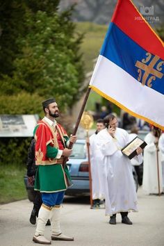 a man holding a flag while walking down the street with other people in white robes