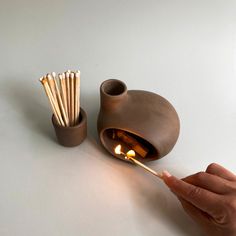 a person holding a match stick in front of a brown cup with matches sticking out of it