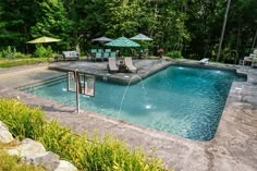 an empty swimming pool surrounded by trees and lawn chairs with umbrellas in the background