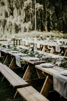 a long table set up with white linens and greenery for an outdoor dinner