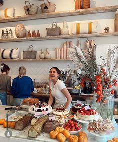 two women standing behind a counter filled with cakes and pastries